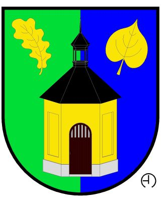 V zeleno - modře polceném štítě zlatá polygonální kaple na stříbrném soklu, s obloukovými dveřmi a střechou s lucernou, vše černé. Nahoře je kaple provázena kosmým dubovým a šikmým lipovým listem, oba vztyčené a zlaté. Znak Buš